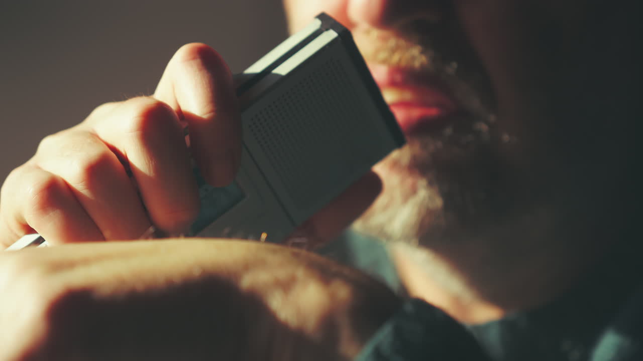 Blurred middle-aged man speaking into analogue dictaphone in dim room. Useful for journalism visuals, investigation scenes, interviews and audio recording themes
