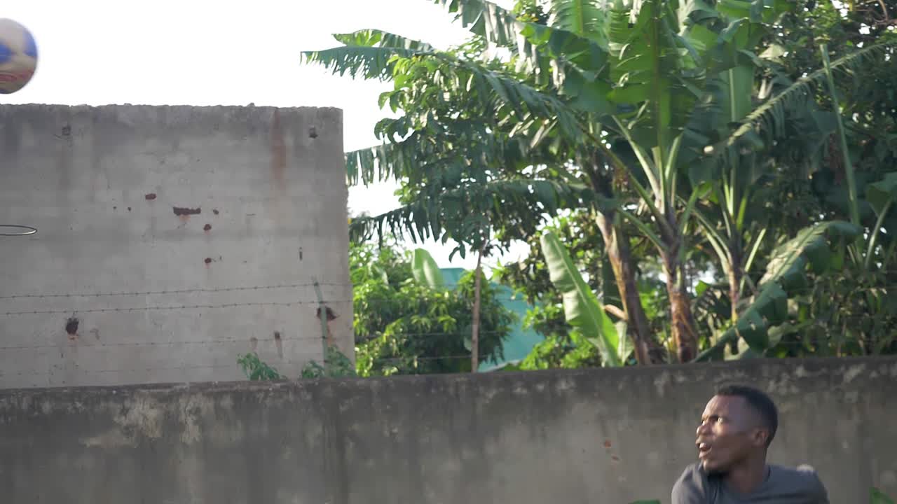 A wide slow motion shot of an African youth spiking a volleyball over a net in rural Africa