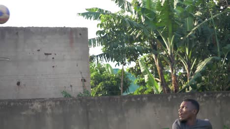 a wide slow motion shot of an african youth spiking a volleyball over a net in rural africa