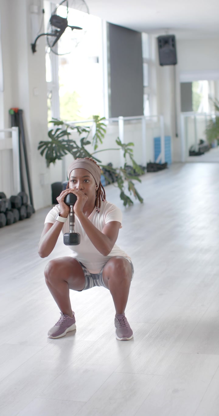 Video verticale: Donna che esegue goblet squat con manubrio al petto in palestra, indossando pantaloncini da fitness.
