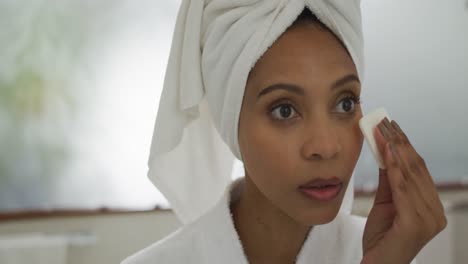 mixed race woman wearing bathrobe cleaning her face