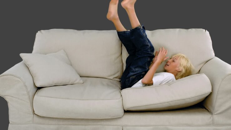 Young boy jumping on the sofa on grey background