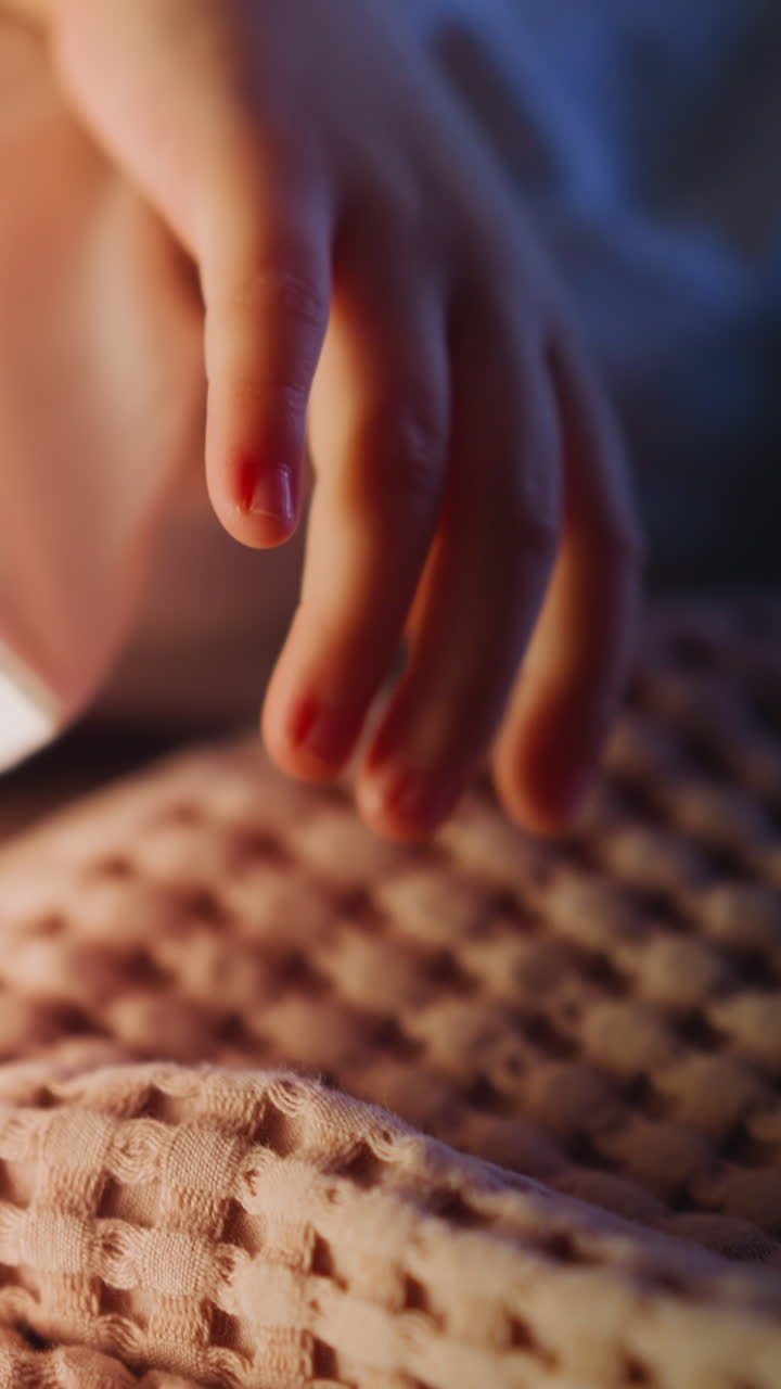 Hand of little kid takes lifting large pillow in white case on bed covered with warm woolen blanket in semidark bedroom at night extreme closeup slow motion