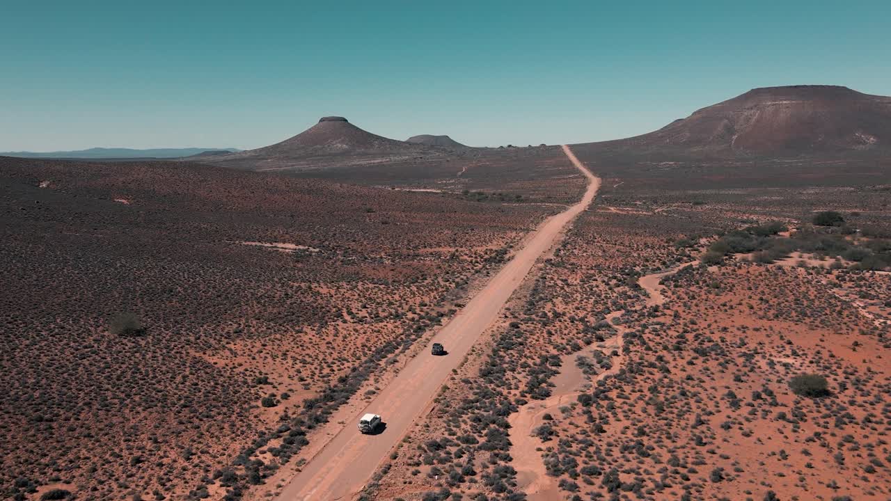 Two cars drive in convoy over a vast landscape in the Karoo of South Africa