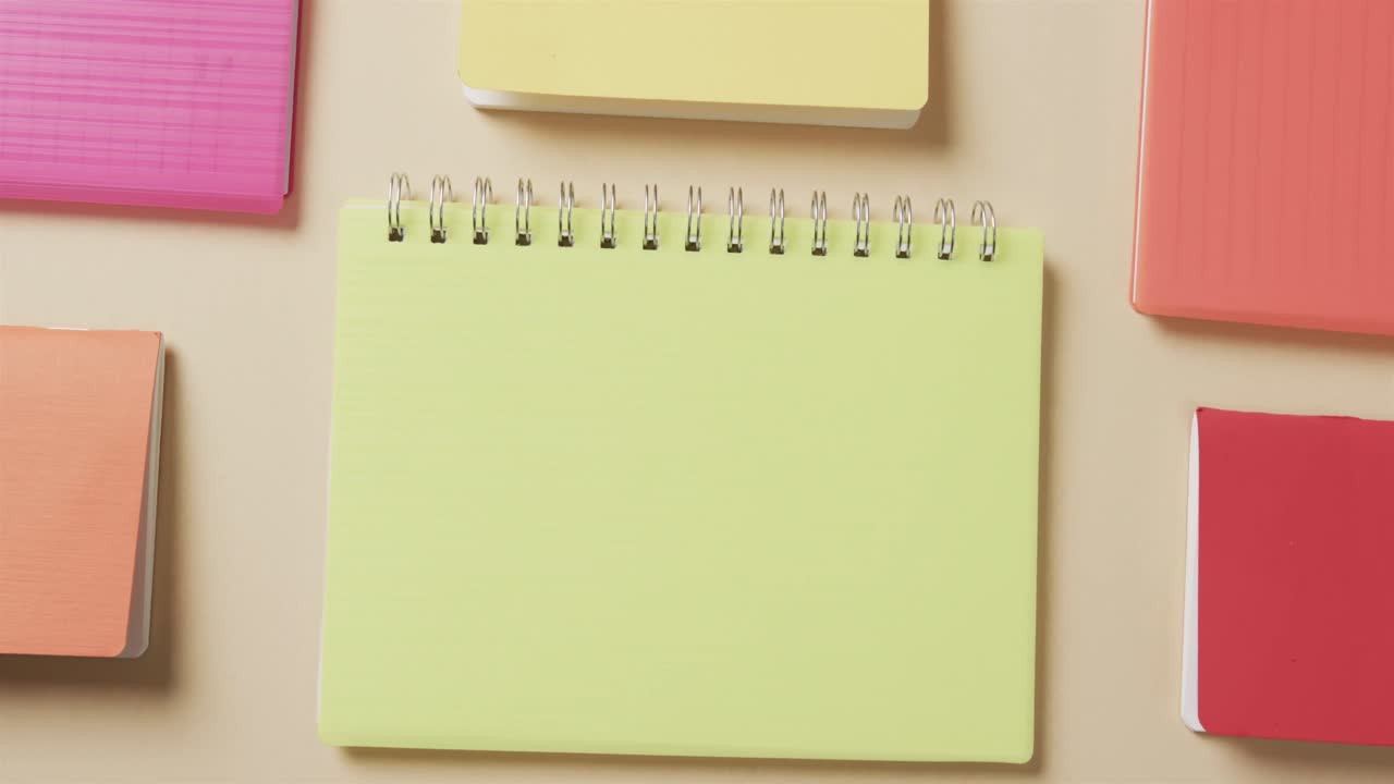 Overhead view of colourful notebooks arranged on beige background, in slow motion