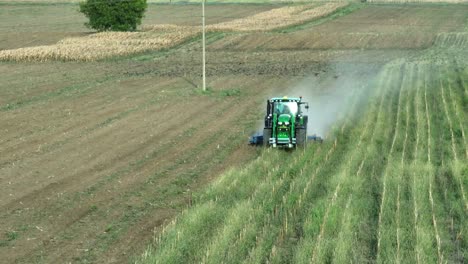 tractor cosechando campo verde durante la luz del sol en la naturaleza - bandada de pájaros siguiendo la maquinaria - vista aérea
