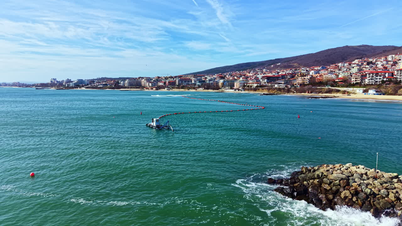 Una barca si muove su acqua limpida vicino a una spiaggia con edifici su una collina sullo sfondo durante una giornata di sole in una zona costiera.