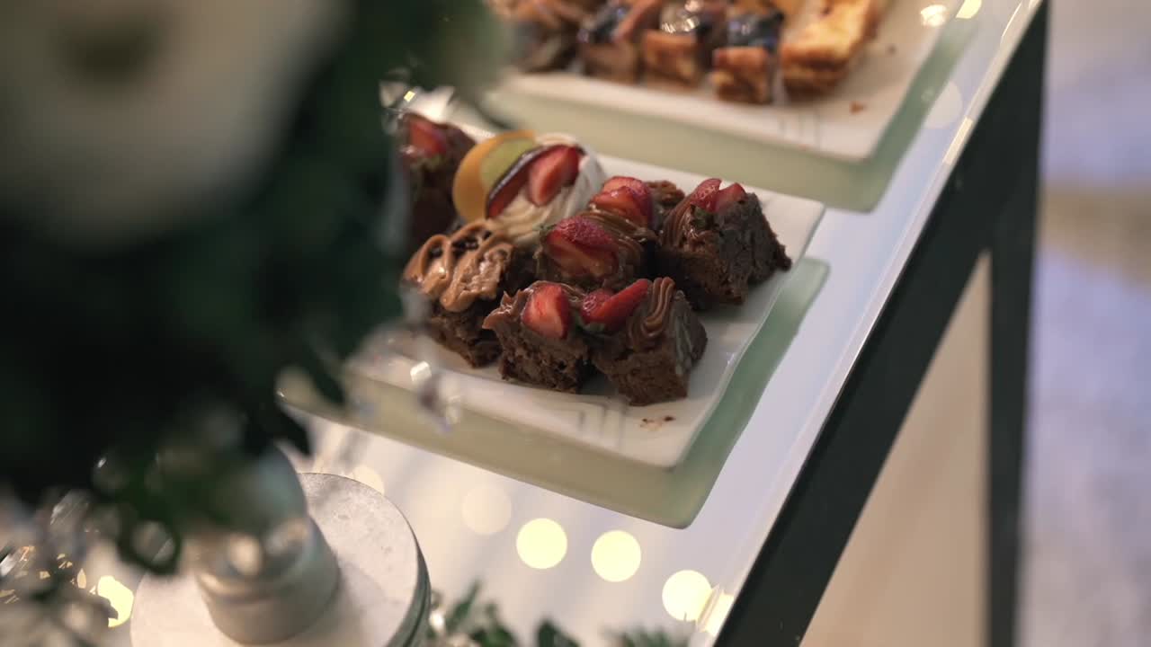 Piatto di mini brownie gourmet e pasticceria elegante con cioccolato, fragole e panna, artisticamente disposti su un tavolo da dessert sofisticato per eventi di lusso e catering, slow reveal