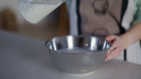 woman pouring milk into metal bowl and making dough