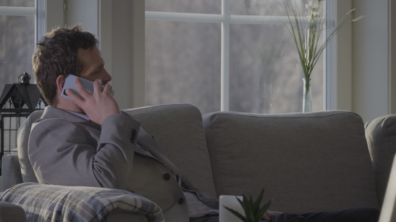 бизнесмен принимает звонок, сидя на диване у себя дома, статичный вид