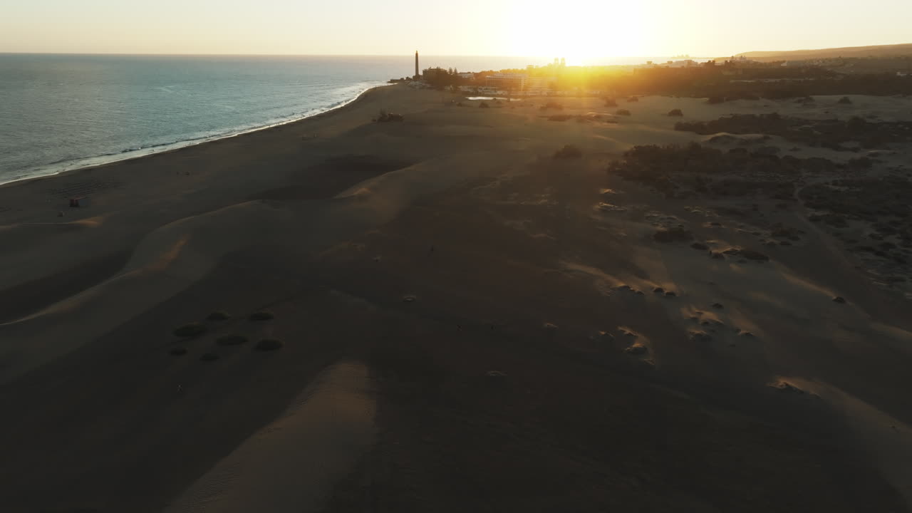 vista aérea recorriendo las dunas de maspalomas durante la puesta de sol y viendo la orilla de la playa