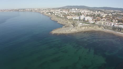 Vista-Aérea-De-Drones-De-La-Playa-De-Estoril-En-Sao-Pedro-Do-Estoril,-Mayor-Lisboa,-Cascais-En-El-Fondo