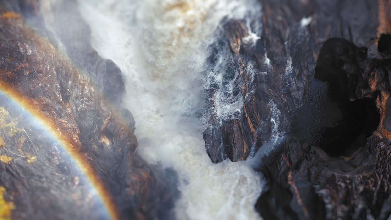 imágenes de la naturaleza que muestran el agua blanca de una cascada cayendo por un acantilado, con niebla y rocas, y el arco iris emerge en el chorro de agua