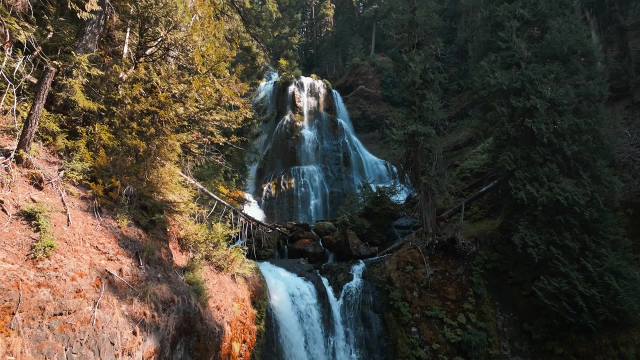 Lenta ripresa aerea in allontanamento che mostra le cascate superiori e inferiori di Falls Creek Falls in un canyon boscoso ombreggiato, circondato da superfici rocciose e alberi.