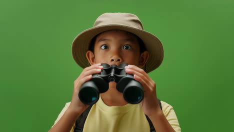 young boy explorer with binoculars and surprised expression on green screen