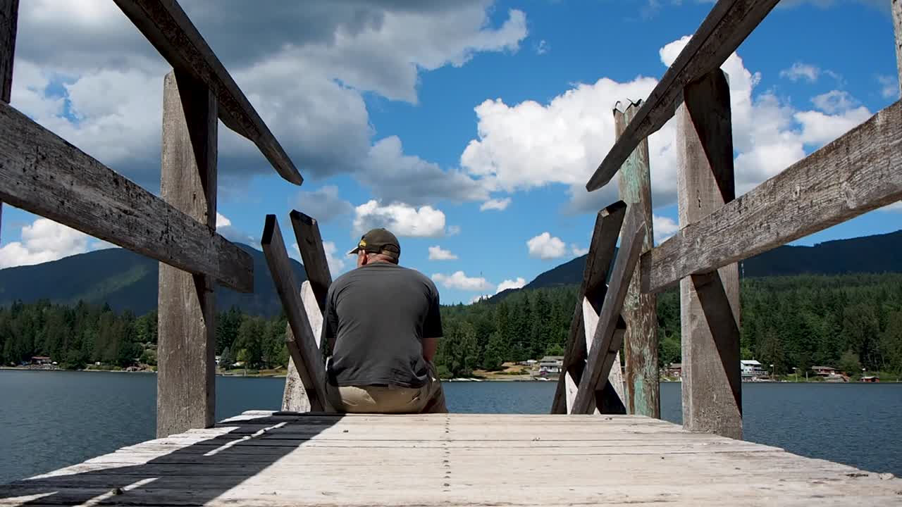 hombre en un muelle de madera en un lago mirando la vista del lago y el cielo