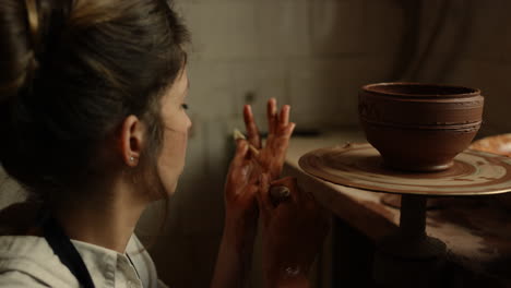 focused woman decorating clay pot in pottery