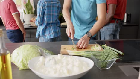 sección media de un grupo diverso de amigos preparando la comida, cortando verduras en la cocina, cámara lenta