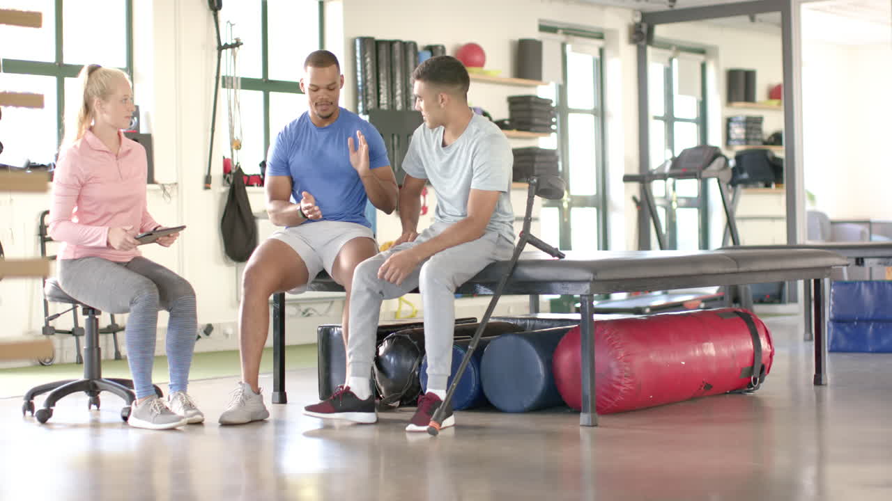 Physical therapist discussing rehabilitation exercises with two men in gym