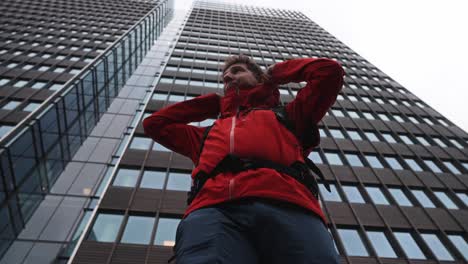 strong man in red jacket and backpack standing tall near skyscraper in urban scene
