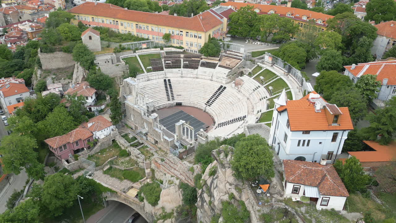 A stunning drone orbit view of the Ancient Roman Theatre in Plovdiv, Bulgaria, captured in early spring with cars passing through the tunnel below