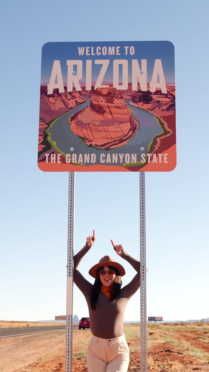 Mujer joven posando bajo el letrero estatal "Welcome to Arizona"