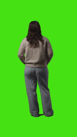 Vertical-Video-Rear-View-Full-Length-Shot-Of-Casually-Dressed-Young-Woman-Standing-And-Waiting-Against-Green-Screen