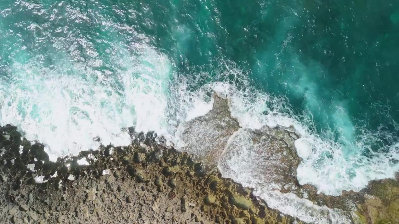 Vista aerea dall'alto di onde caraibiche turchesi che si infrangono contro una costa rocciosa frastagliata a Watamula, a Curaçao, rivelando schiuma drammatica e roccia corallina aspra.