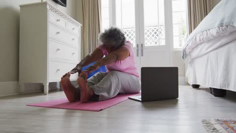 Senior african american woman performing stretching exercise while looking at laptop at home