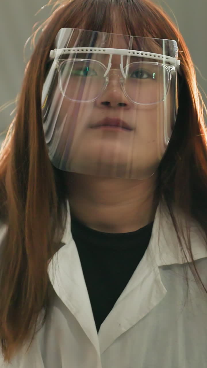 técnico de laboratorio con escudo facial observa un coche levantado mientras toma notas en una computadora portátil en un taller mecánico, el fondo presenta herramientas industriales, equipos mecánicos y espacio de trabajo estructurado