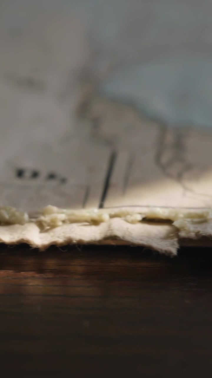 Vertical video: Camera pulling, revealing off white torn sheet on wood table with frayed edge, bits