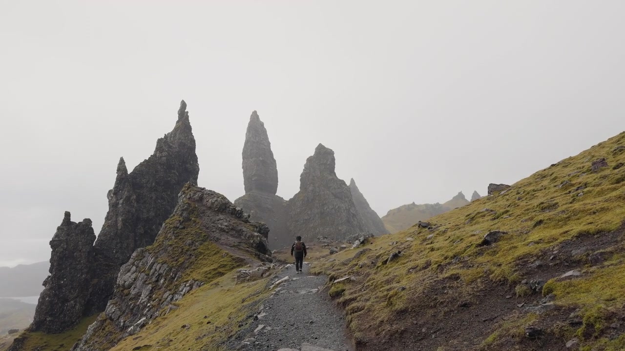 The Storr, Skotsko, turista kráčí po úzké stezce vedoucí k skalnatým vrcholům s mlhavou atmosférou ve Skotské vysočině.