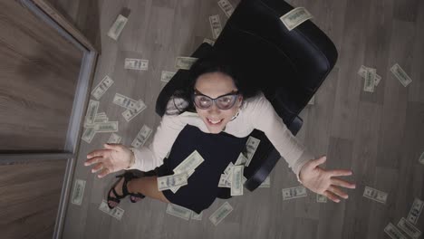 top view cheerful, smiling and a little crazy young brunette wearing white blouse and black skirt sitting on office chair. happy  manager or secretary. dollars falling on her from above