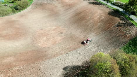 A tractor working in a field, driving uphill among the trees of the forest seen from a drone&#039;s perspective