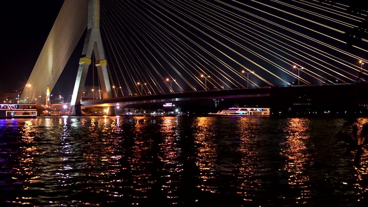 전선 다리 아래의 강에 조명을 탑재한 레크리에이션 보트가 배치되어 있습니다.