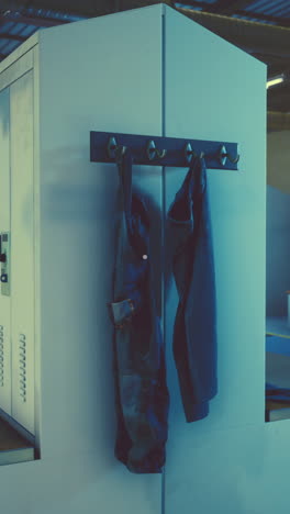 blue and grey workwear hangs on hooks next to metal lockers.