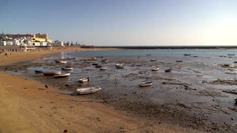 Menschen-Erkunden-Den-Strand-Bei-Ebbe-Mit-Kleinen-Fischerbooten-Im-Wasser