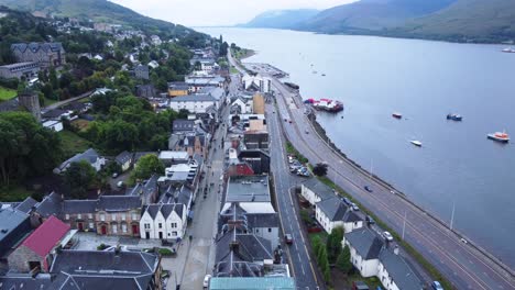 cars driving along road near loch in fort william town, west highland museum, town centre - aerial drone 4k hd footage rise up