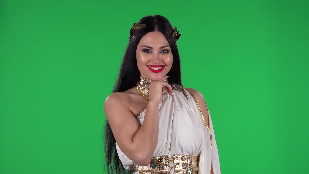 Ritratto di bella donna in abito da dea greca e ghirlanda di alta moda, che guarda dritto e agita la mano mostrando il gesto "vieni qui". Green screen.