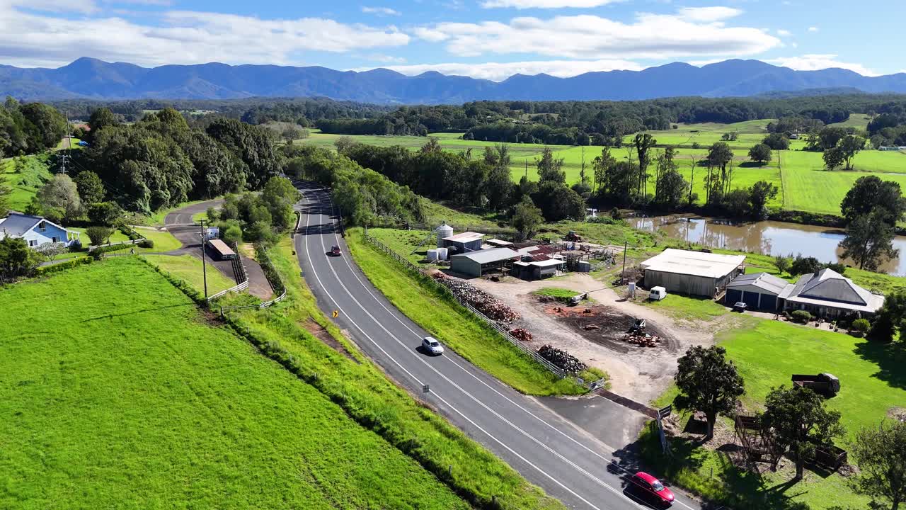 Aerial footage captures a winding road through lush green fields in Bellingen, NSW, under clear blue skies