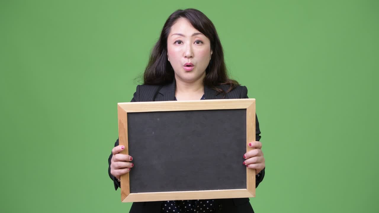 성숙 한 아름다운 아시아 사업가 는 블랙보드 를 보여주는 동안 충격 을 느끼고 있다