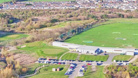 aerial view of waterfront golf club driving range facility with car park and suburban homes in the background, lush green environment, morning light, rotherham, uk