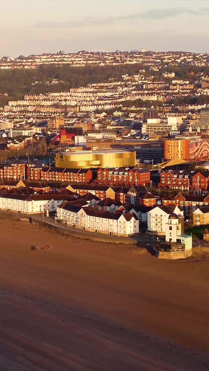 Video verticale, vista aerea della Baia di Swansea con l'Arena e le case urbane circostanti durante una splendida alba. Seconda città più grande del Galles, Regno Unito. Formato 9:16 per i reel dei social media