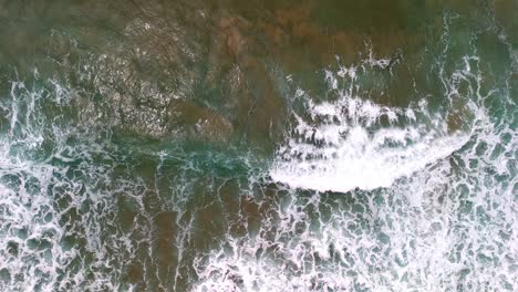 Vista-Aérea-De-Una-Ola-Rompiendo-En-Una-Playa-De-Arena-Dorada,-Los-Fascinantes-Patrones-De-Espuma-Y-Surf