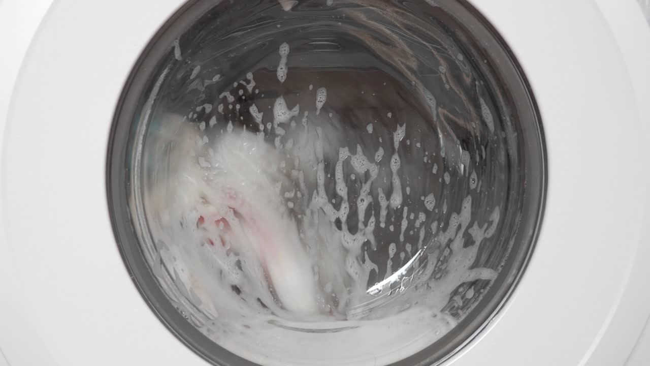 Working washing machine, front view with door and foam by laundry detergent, video 4k resolution