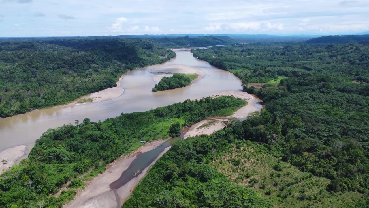 Aerial drone view of a wide meandering Amazon river with pale sandbanks and small islands curving through dense rainforest in Ecuador on a sunny day.
