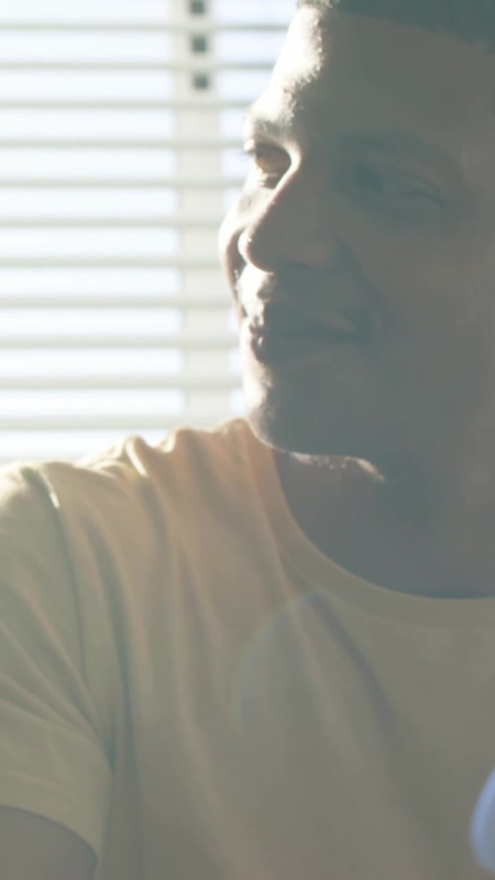 Vertical video: Turning man smiling and listening to woman on couch after pan with blinds, pale tee