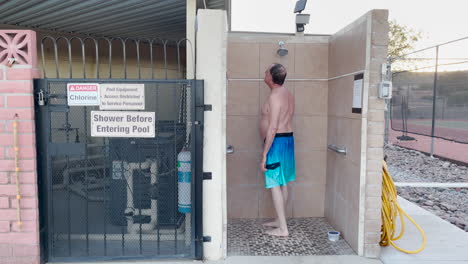 un anciano se da una ducha al aire libre antes de entrar a la piscina.