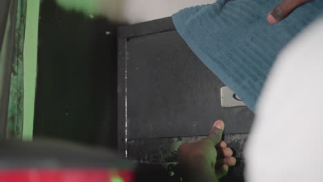 close-up of person in white shirt reaching up to place blue cloth in storage cabinet with worn surface in dimly lit room. hand carefully adjusts cloth, focusing on organization and tidiness