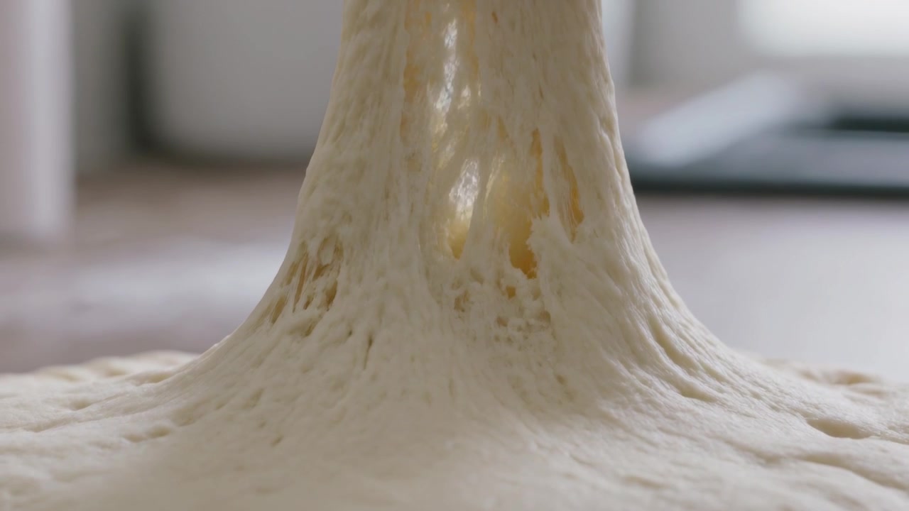 Pressing thumb, home baker's hand pinching and lifting proofed dough on countertop, testing gluten
